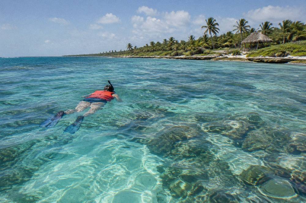 A snorkeler in a life vest floating over a shallow coral reef in clear blue water