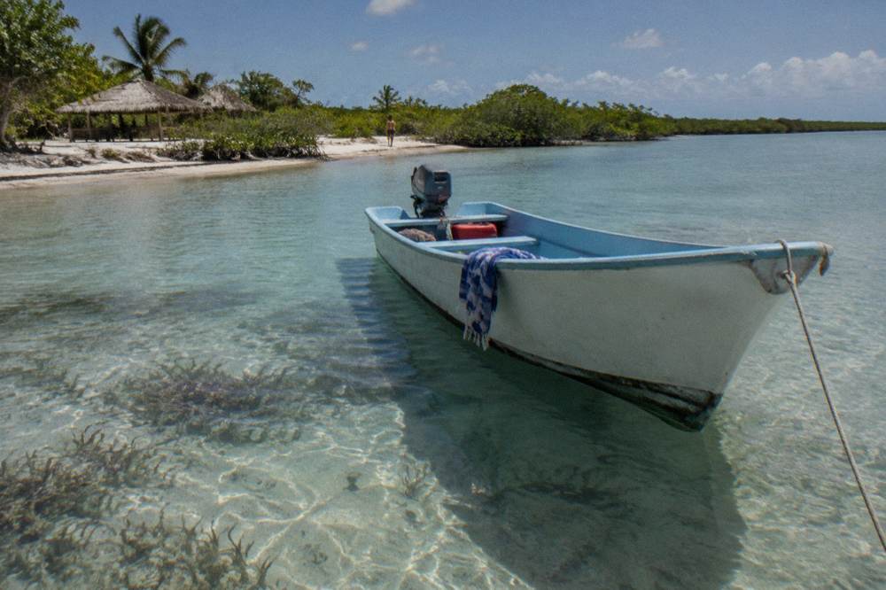 A small boat anchored beside a shallow sandy natural pool in turquoise lagoon water