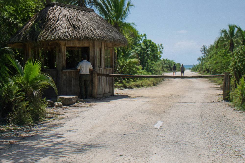 A small wooden checkpoint hut beside a gravel track with tropical forest on both sides