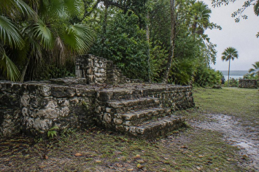 A small stone Maya ruin on a grassy clearing surrounded by low jungle