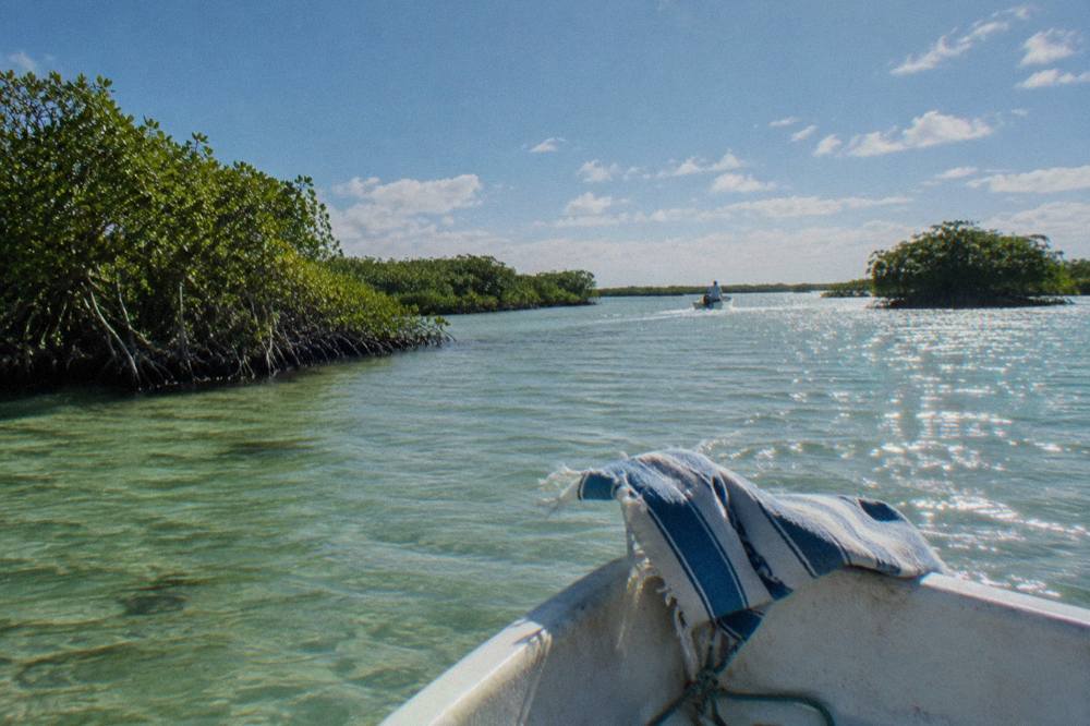 A small open boat crossing a wide shallow lagoon with mangrove islands under a bright sky