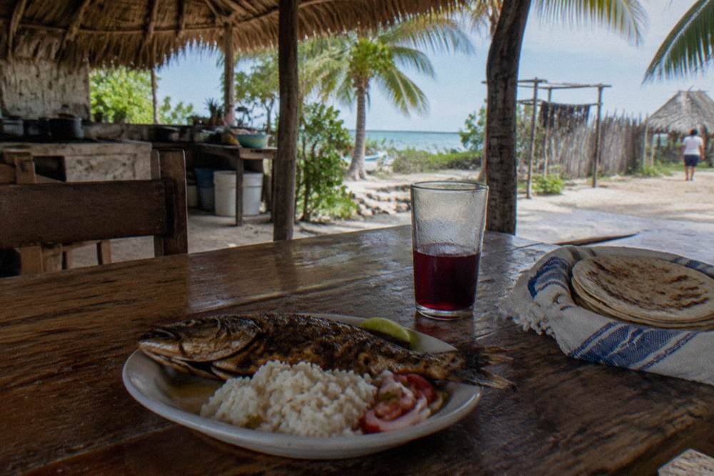 A plate of fresh fish and rice served on a wooden table at a village kitchen.