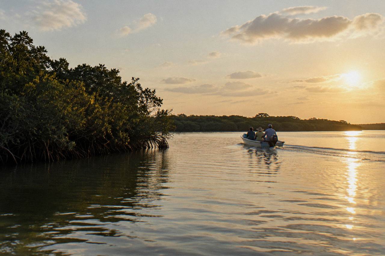 A small boat crossing a calm lagoon lined with mangroves under a wide sky in Sian Ka'an.