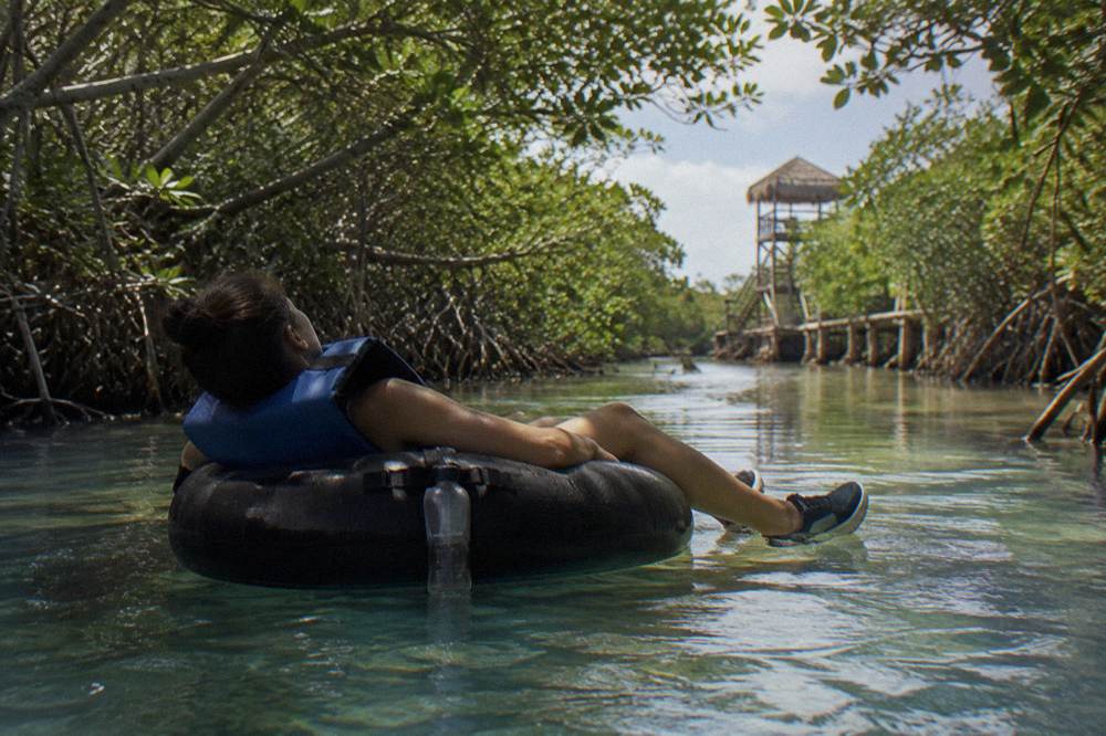 Person reclined in a life vest drifting along a narrow tree lined canal