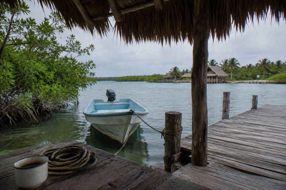 Small wooden boat moored at a lagoon dock beside a thatched palapa shelter