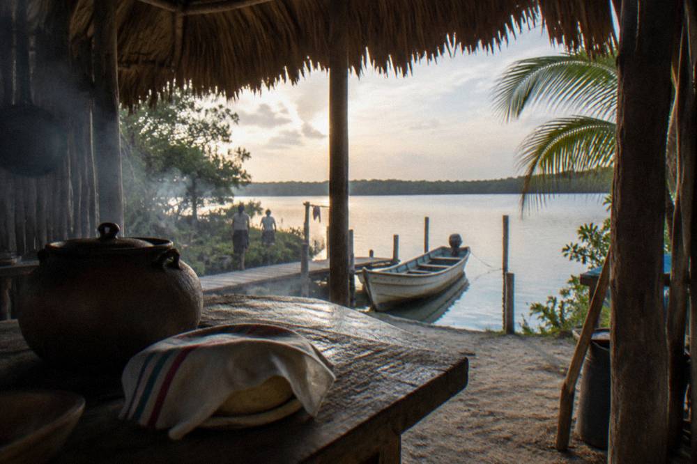Small wooden boat moored at a lagoon dock beside a thatched palapa