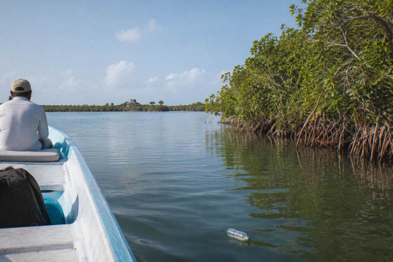 A small boat crossing a wide calm lagoon bordered by mangroves under an open sky