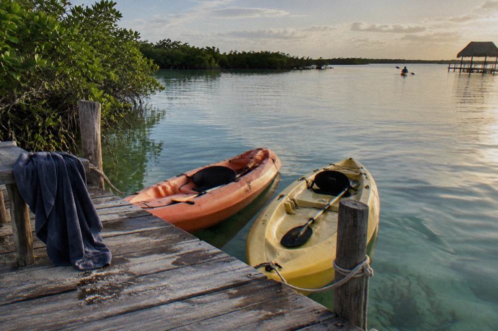 Two kayaks resting on a wooden dock beside still lagoon water in late afternoon light