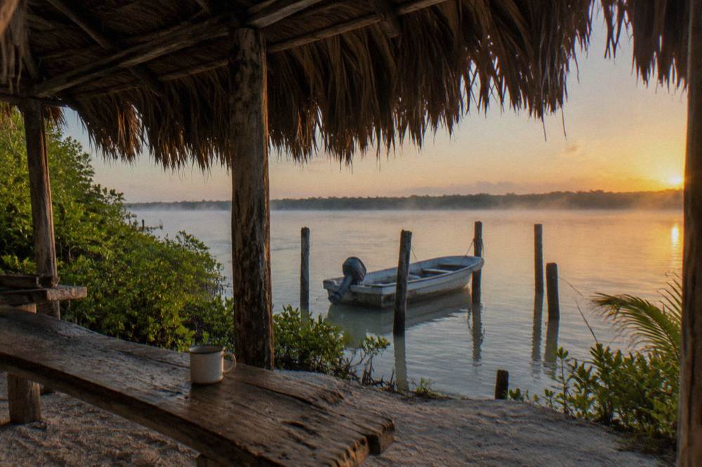 Palm Thatched Palapa Beside A Lagoon With A Small Boat Moored Nearby