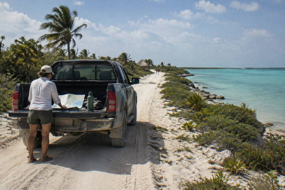 A rugged four wheel drive vehicle on a sandy track beside turquoise lagoon water