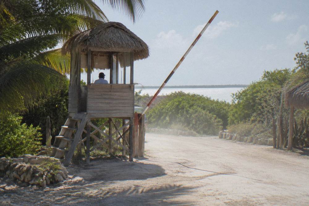 A small wooden checkpoint booth beside a dirt road at the edge of green wetlands