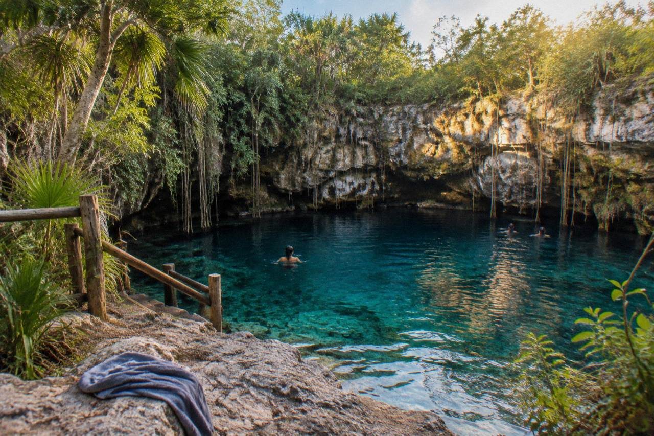 Still turquoise water of a jungle sinkhole ringed by rock and hanging vines