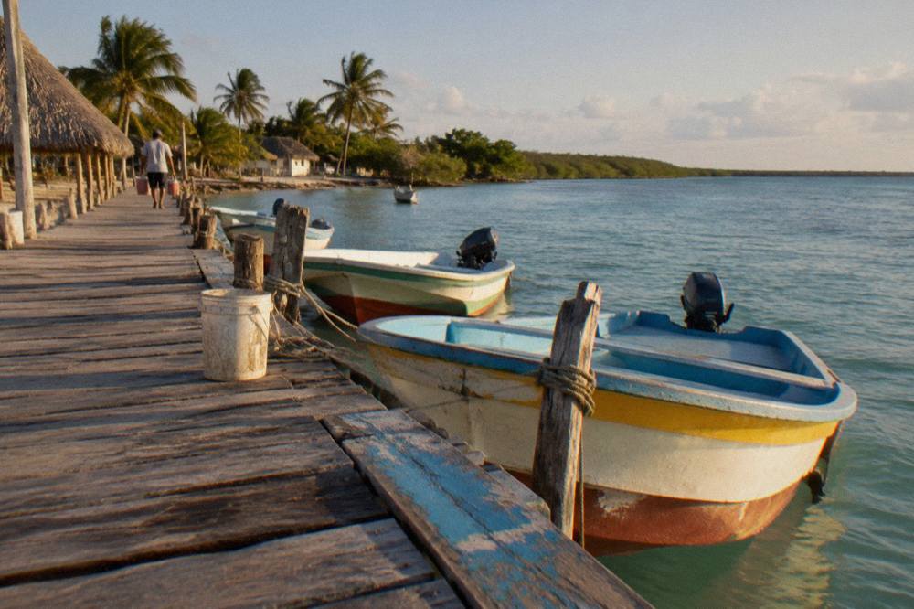 Small colorfully painted boats tied along a wooden dock in a quiet village harbor