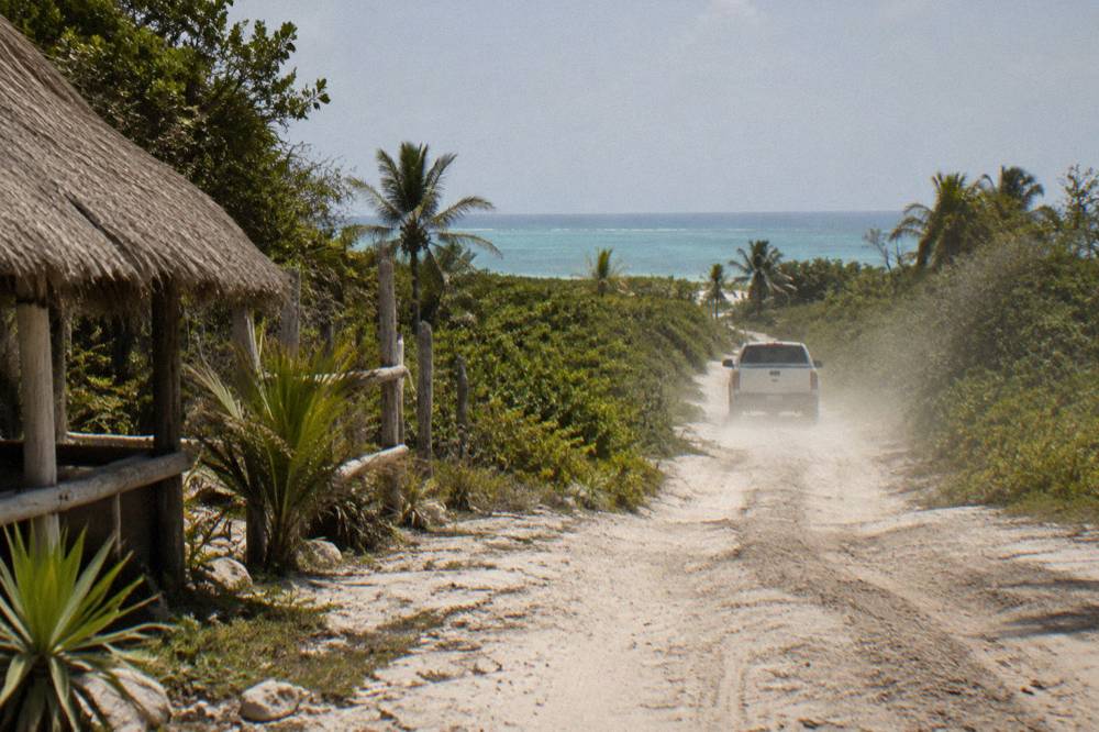 A narrow unpaved dirt track cutting through low jungle toward a distant coastline