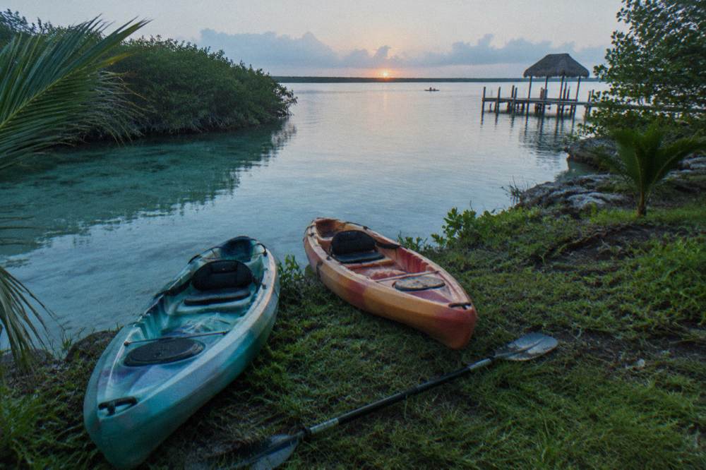 Two kayaks resting on a grassy bank beside clear shallow lagoon water at sunrise