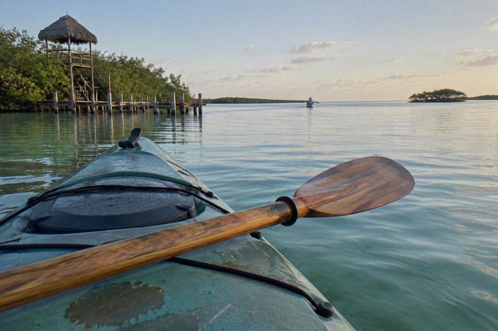 Paddle resting across a kayak deck with pale morning light on distant lagoon water