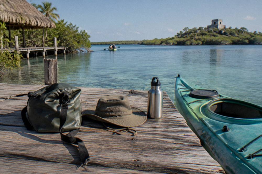 Dry bag, wide-brimmed hat and water bottle laid out beside a kayak on a wooden dock