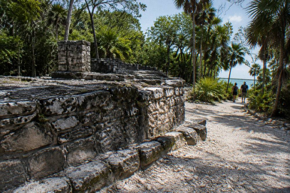 Ancient stone ruin foundation beside a jungle path leading toward open water