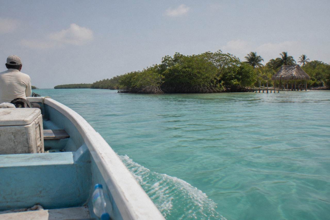 Boat crossing a clear turquoise lagoon toward mangrove islands in a coastal biosphere reserve