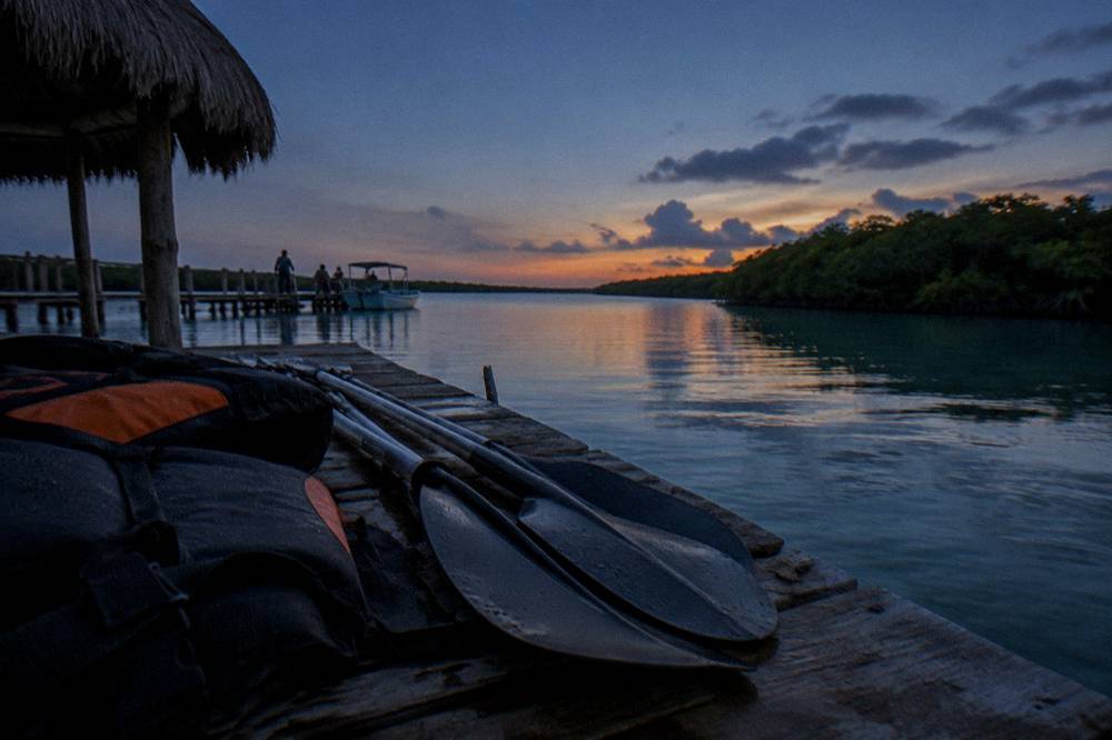 Paddles and life vests stowed on a dock beside calm water at dusk