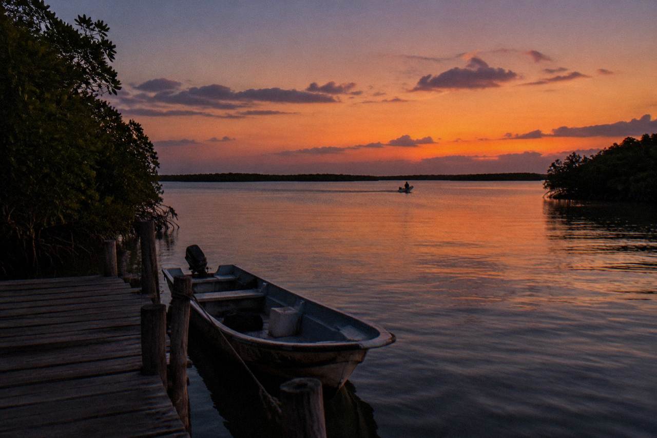 A calm lagoon at dusk with mangrove shoreline under an orange sky
