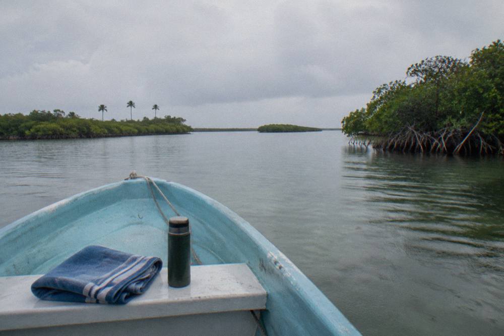 A small open boat crossing a wide calm lagoon with mangrove islands under a pale sky