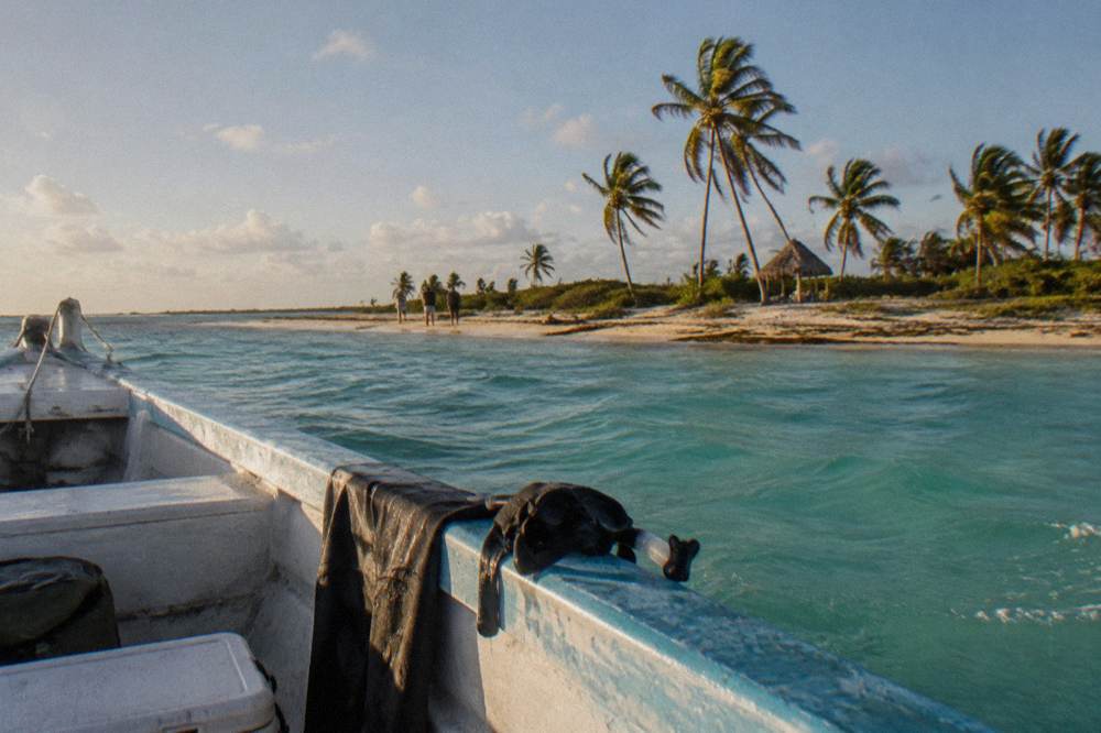 An open boat anchored in shallow turquoise water near a sandy spit with scattered palms