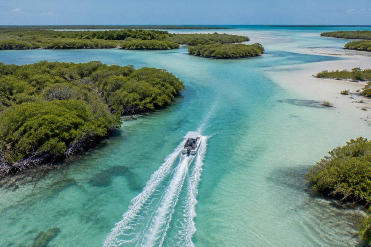 Boat crossing a wide lagoon between mangrove islands under a bright sky