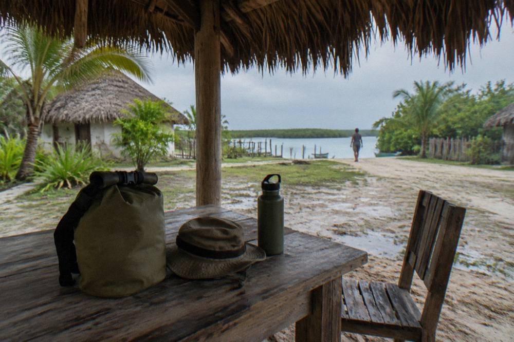 Canvas dry bag, wide-brim hat and water bottle packed on a wooden bench beside a lagoon