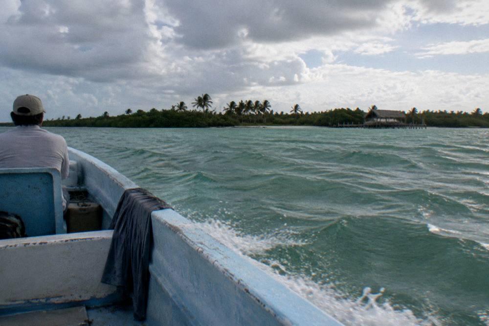 Open boat crossing a wide lagoon towards a distant strip of coastline under broken clouds