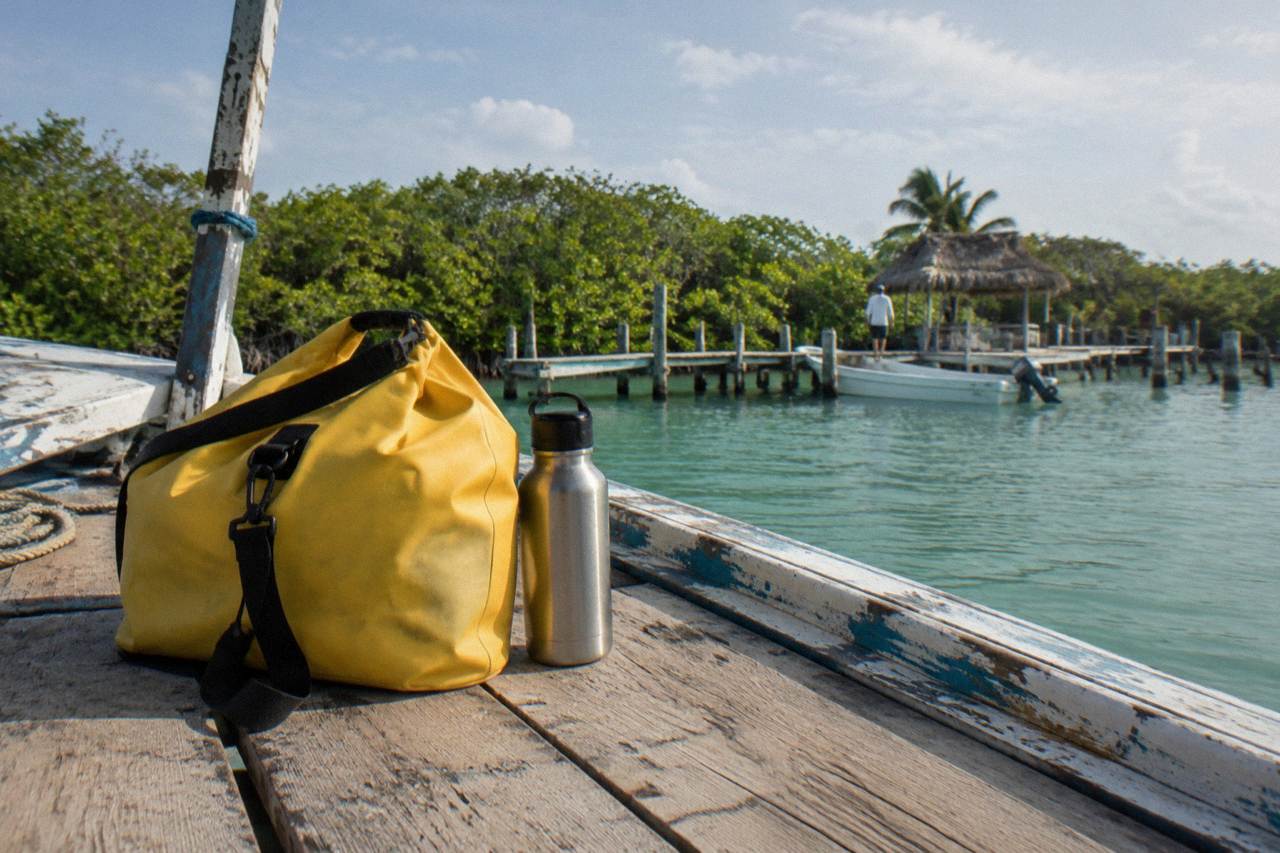 Dry bag and water bottle resting on a wooden boat deck beside lagoon water and mangroves